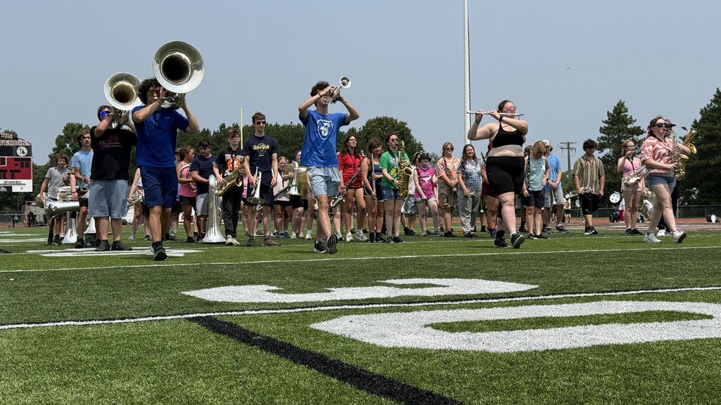 Several band members marching on a football field for practice.