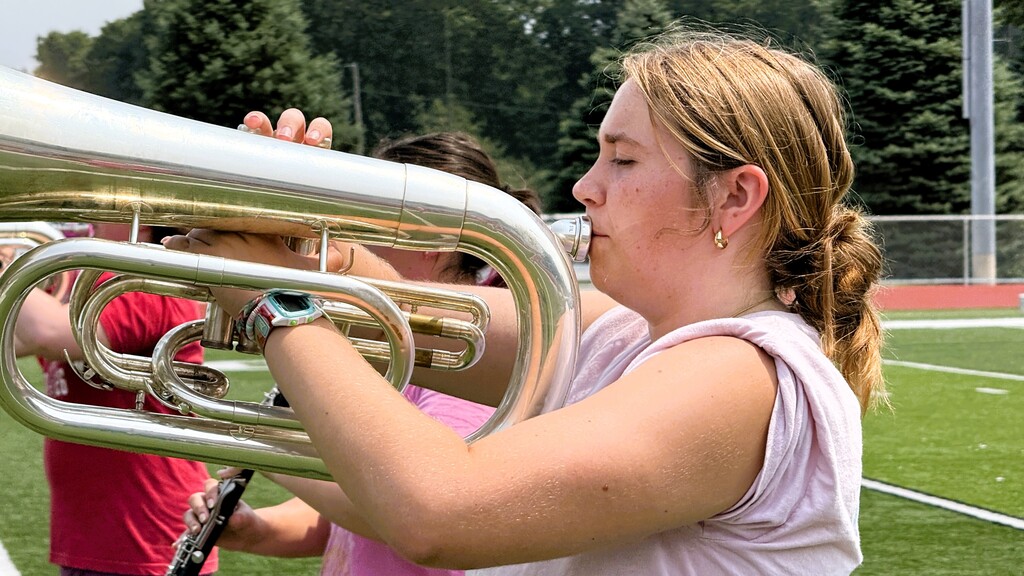 Band member carrying large instrument marching on a football field for practice.