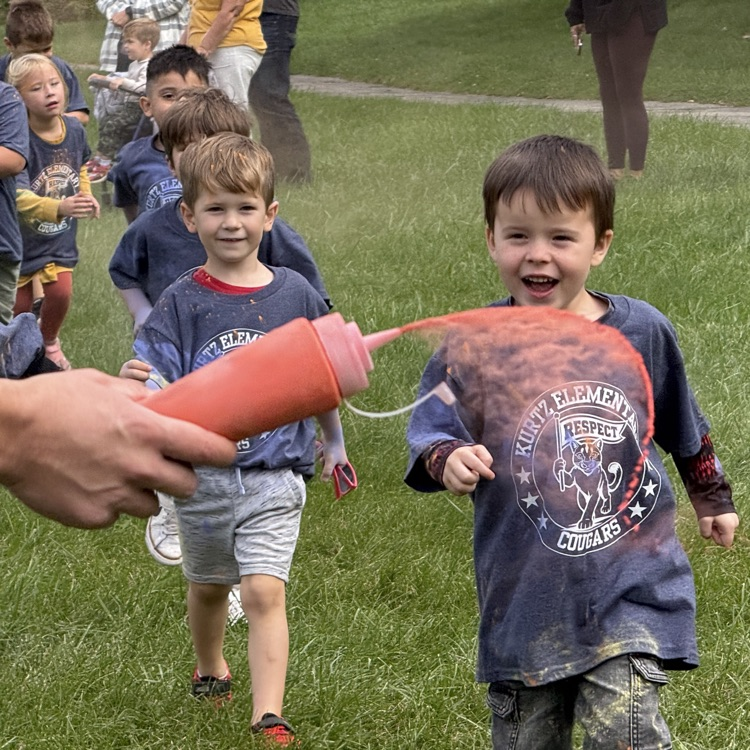 kids running in a field as colorful powder is sprayed at them