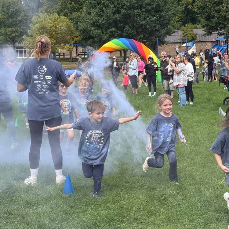 kids running in a field as colorful powder is sprayed at them.