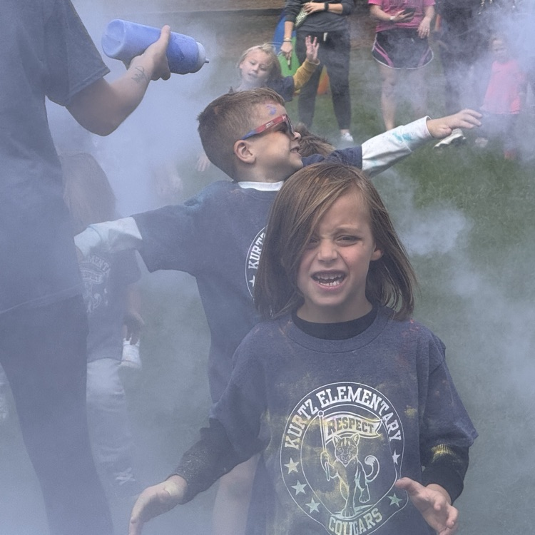 kids running in a field as colorful powder is sprayed at them.