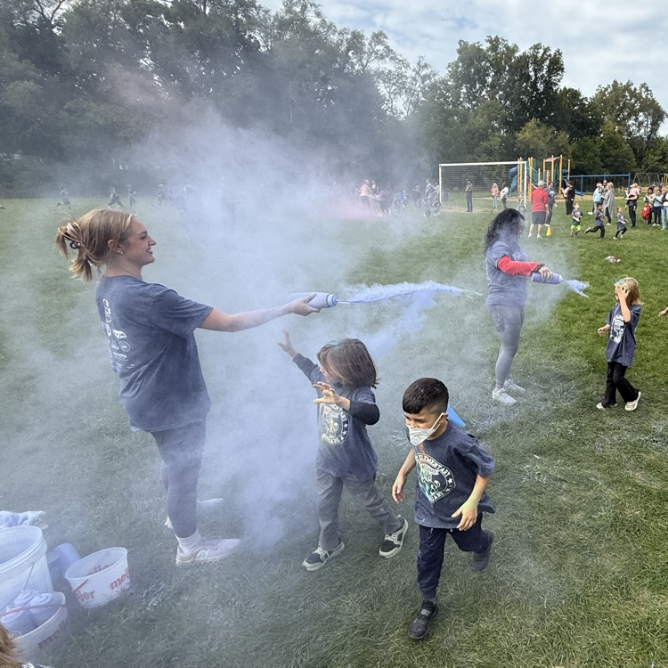 kids running in a field as colorful powder is sprayed at them.