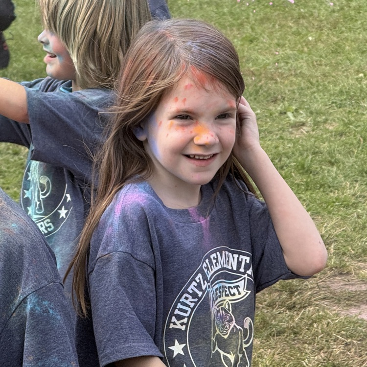 kids running in a field as colorful powder is sprayed at them.