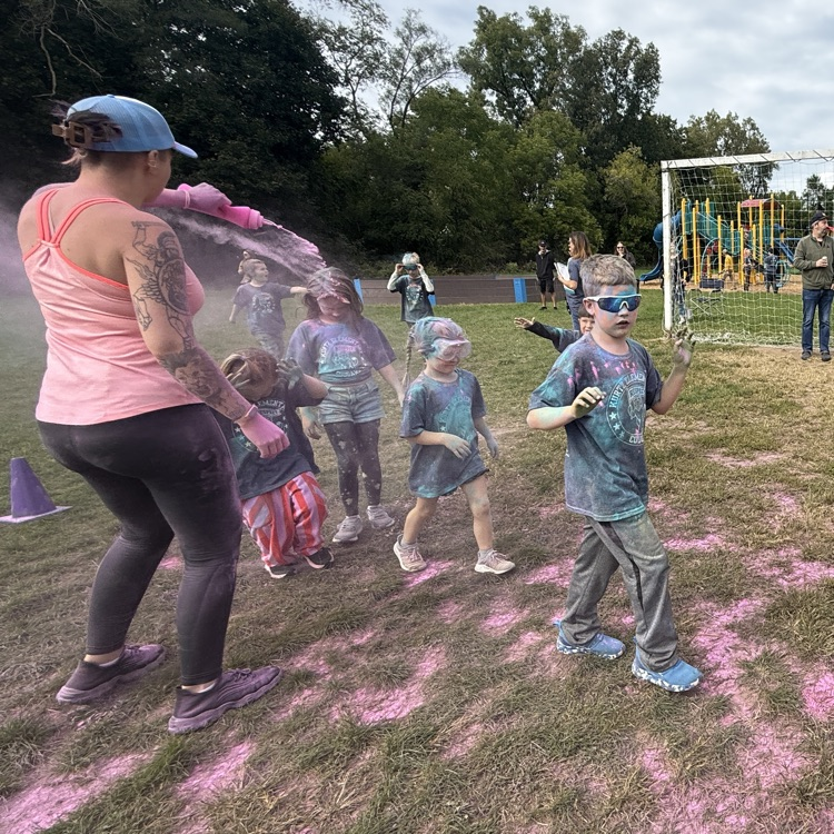 kids running in a field as colorful powder is sprayed at them.