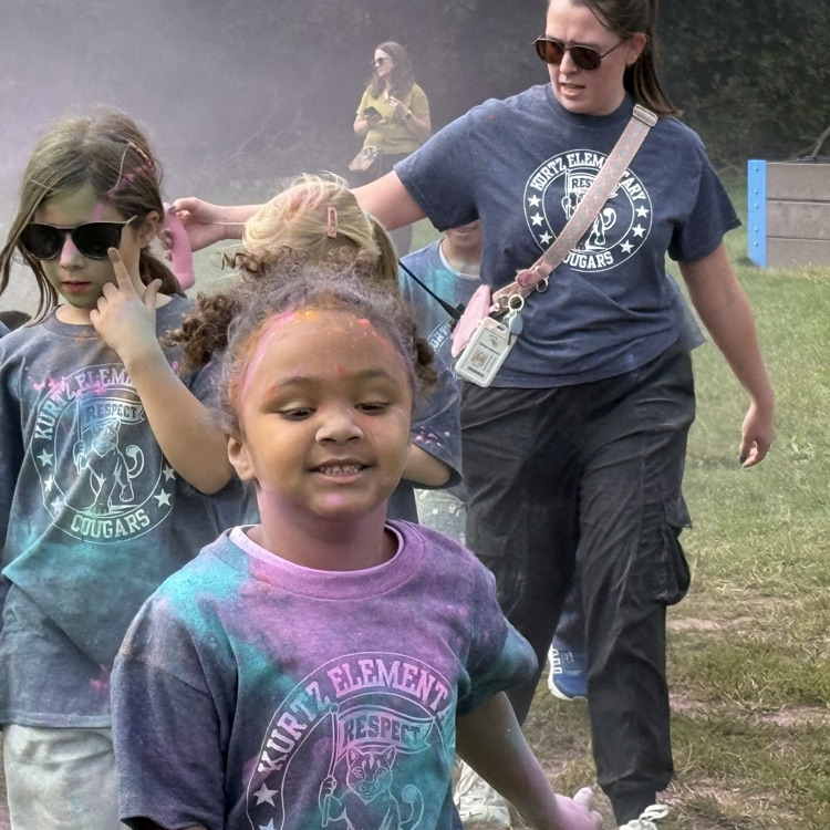 kids running in a field as colorful powder is sprayed at them.