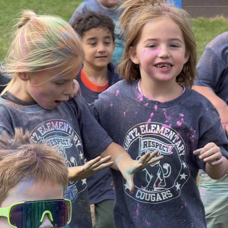 kids running in a field as colorful powder is sprayed at them.