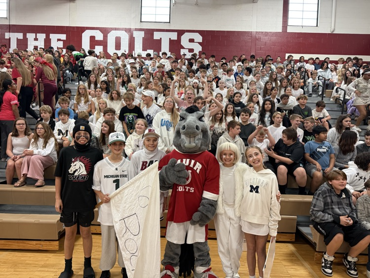 a group of students stand with a mascot in front of bleachers filled with students