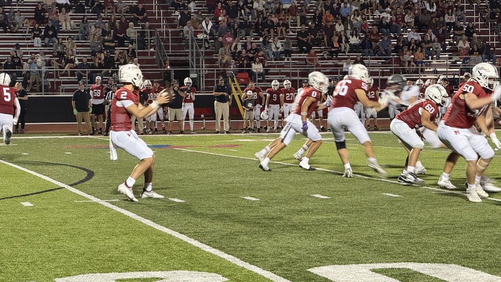 Photo of footbal players hiking the ball as a play begins on a football field