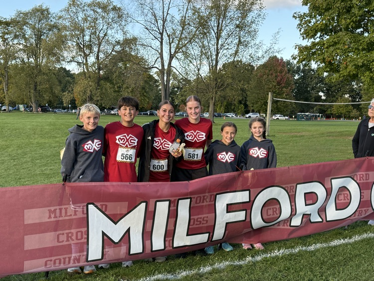 cross country team stands in front of barrier banner that says Milford in red shirts
