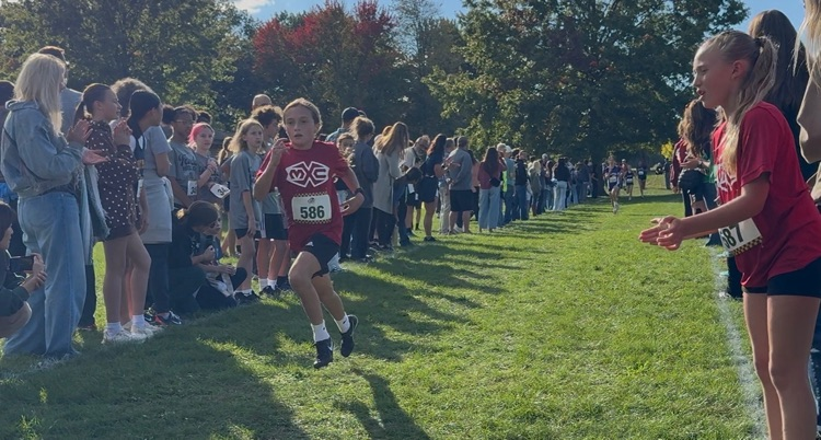 a cross country runner in red Muir jersey getting cheered on 