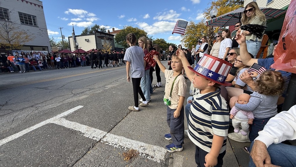 Boy in USA hat waving a flag at a downtown parade.