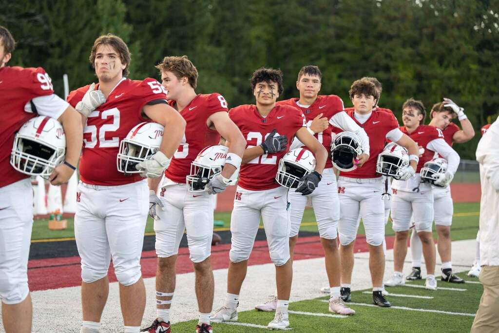 Football players in red uniforms standing on the sidelines for the national anthem