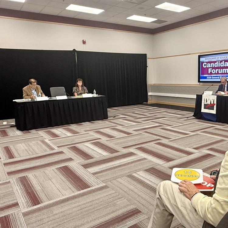 phot of man and woman sitting at table in a conference room with an audience member sitting in front of them