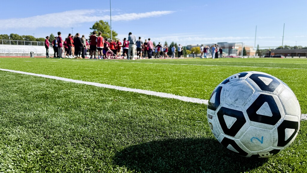 Several soccer players maneuvering for a ball on a field with a soccer ball in the foreground