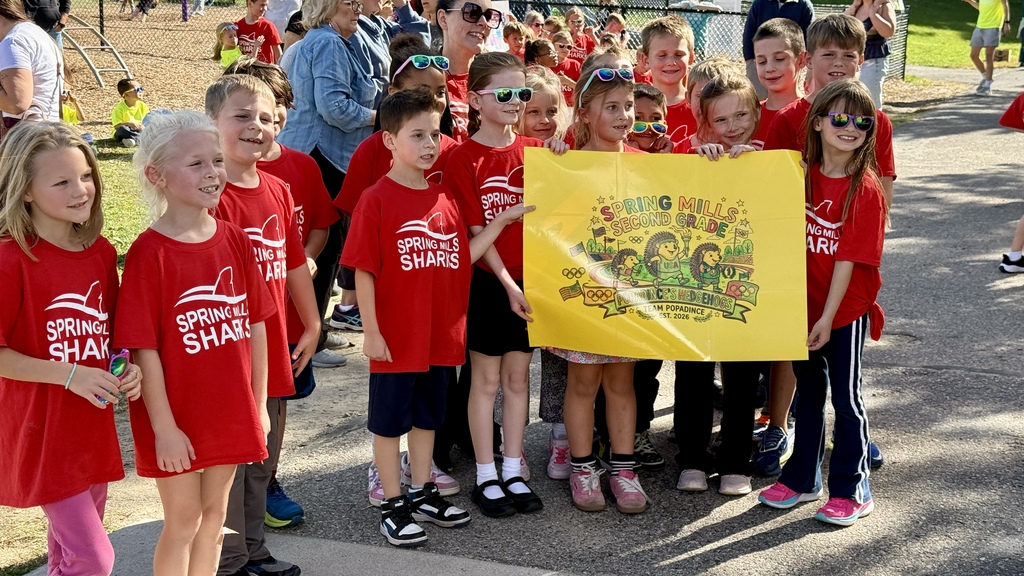 Several students posing for a photo holding a sign while wearing red shirts outside