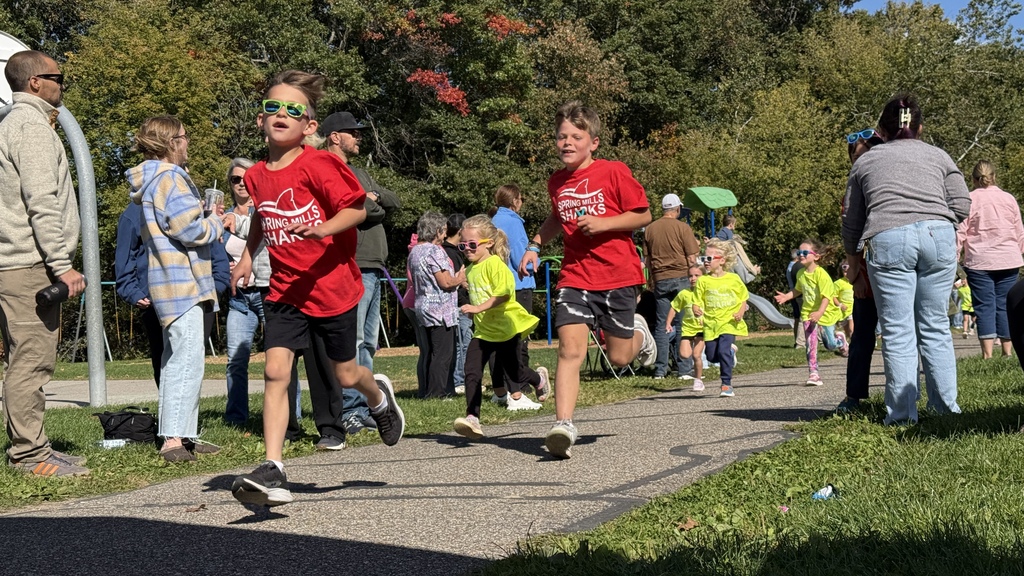 Photo of two kids in red shirts running on a path outside while adults look on