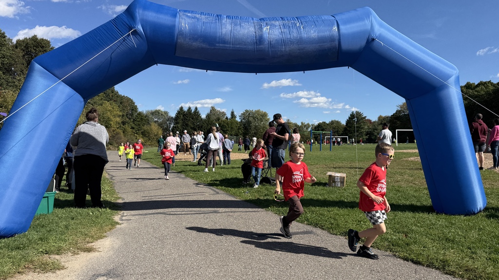 Two kids in red shirts running underneath a blue inflatable arch 