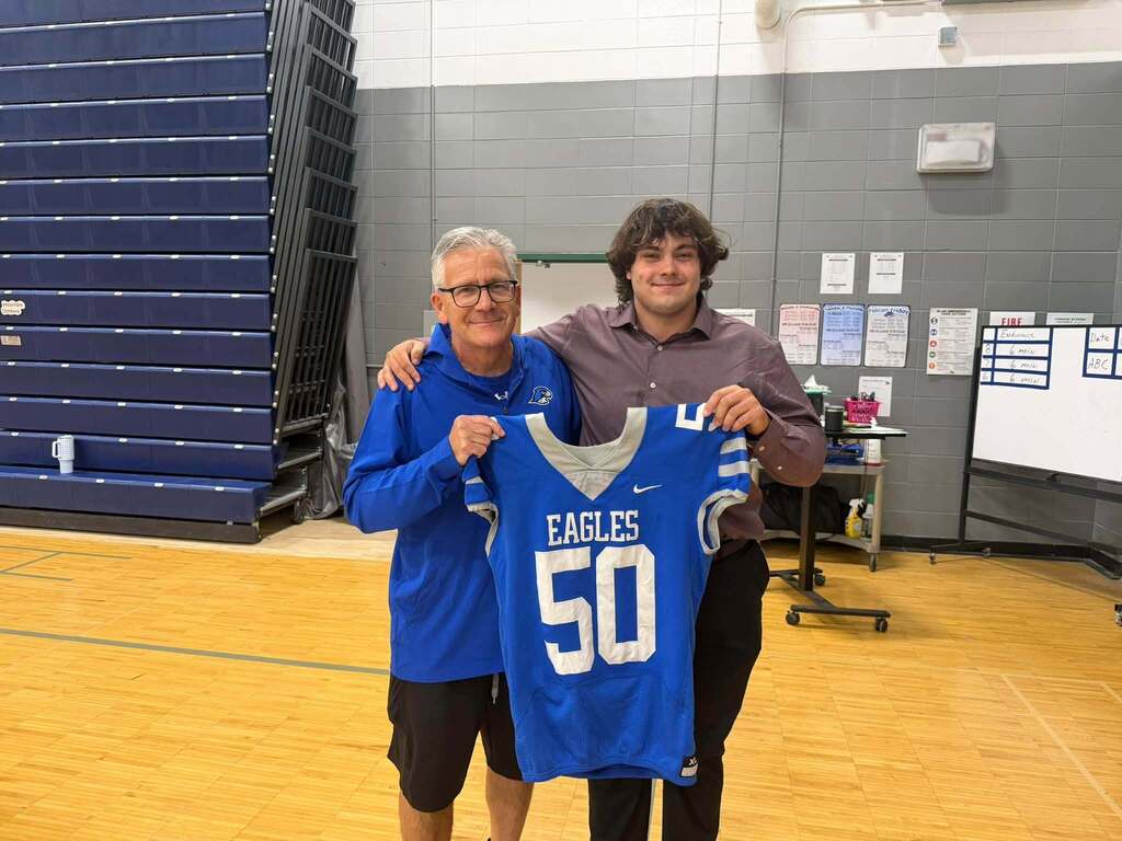 Football players holding jersey posing & smiling for a photo with a teacher