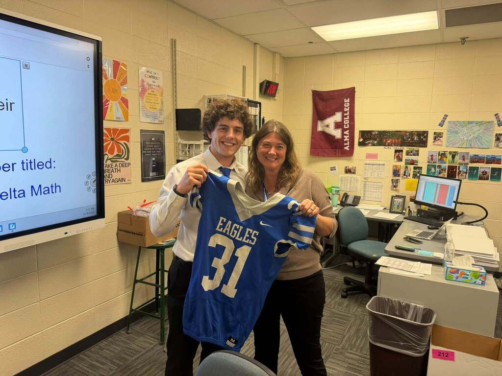 Football players holding jersey posing & smiling for a photo with a teacher