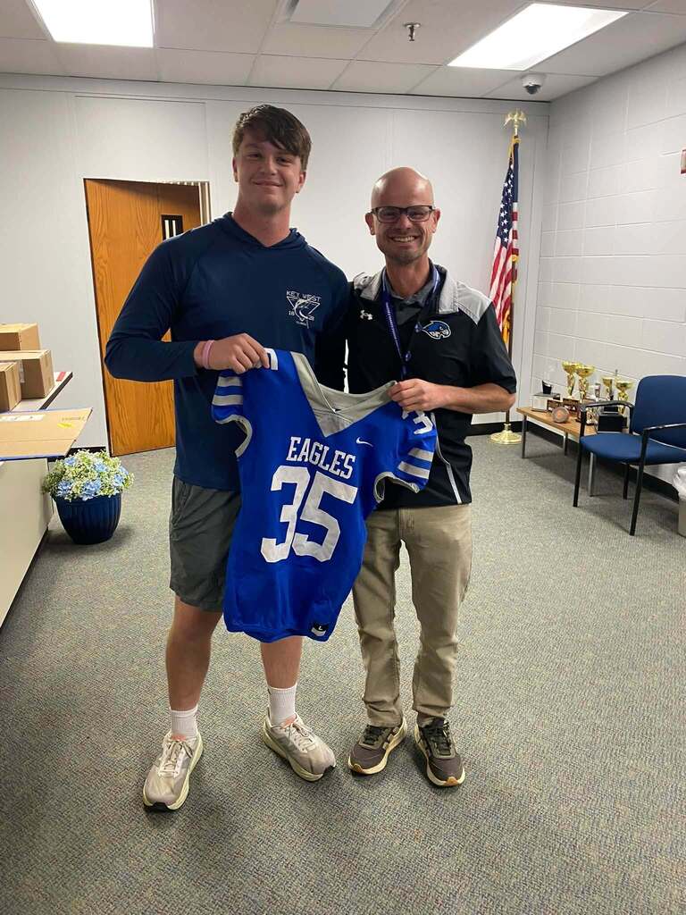 Football players holding jersey posing & smiling for a photo with a teacher
