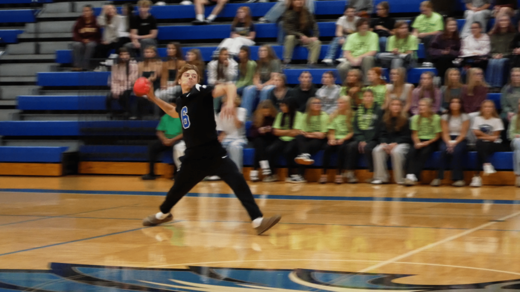 Male student winding up to floor a ball on the gym floor as the crowd watches