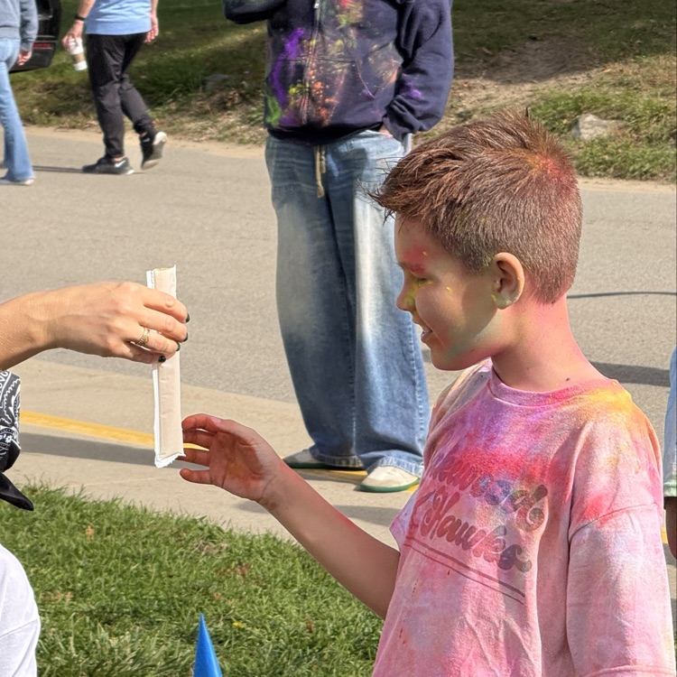 child covered in colored powder being handed a popsicle