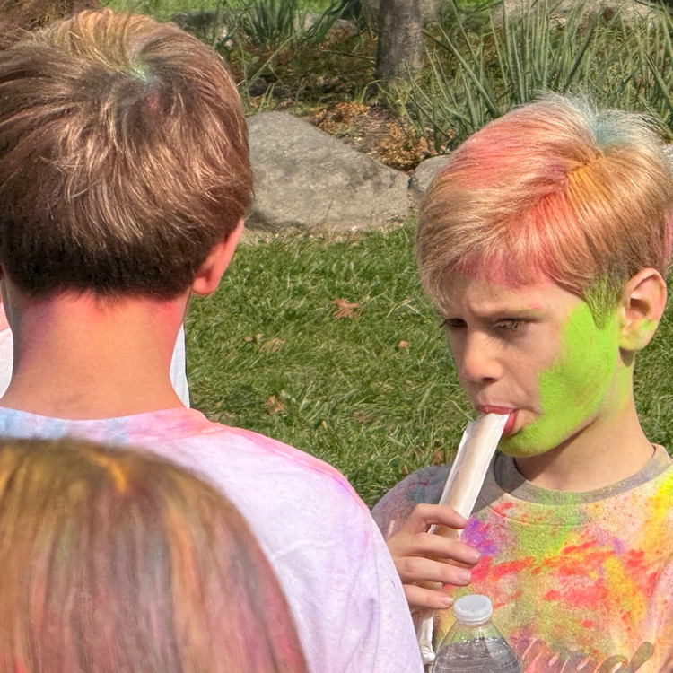 child covered in colored powder being handed a popsicle