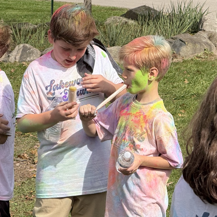 child covered in colored powder being handed a popsicle