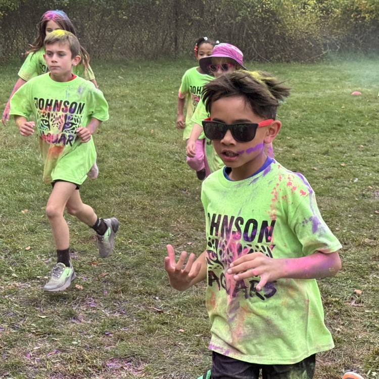 young students running with colored powder being tossed at them in a field
