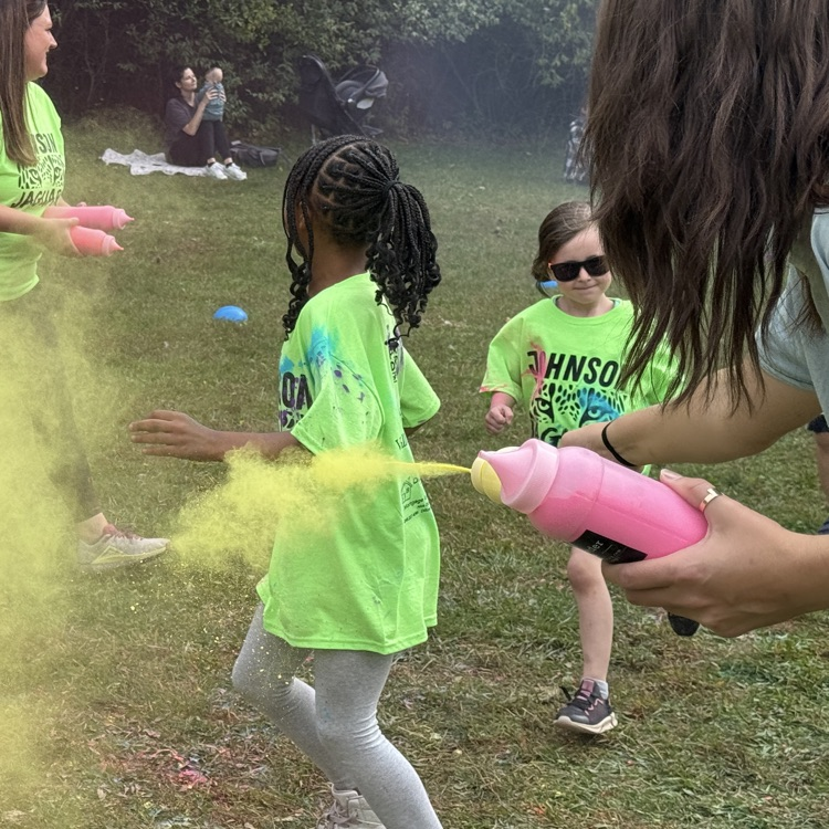 young students running with colored powder being tossed at them in a field