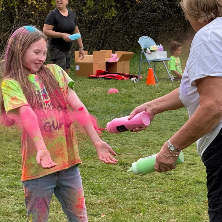 young students running with colored powder being tossed at them in a field