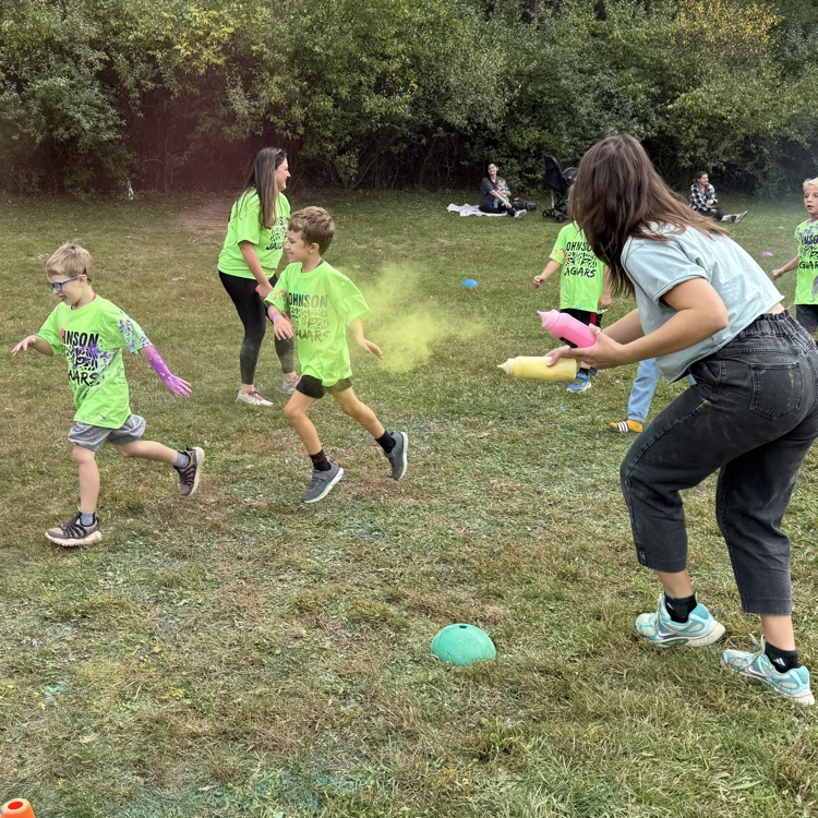 young students running with colored powder being tossed at them in a field