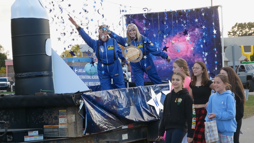 Parade float withg two people dressed as astronauts on top of it 