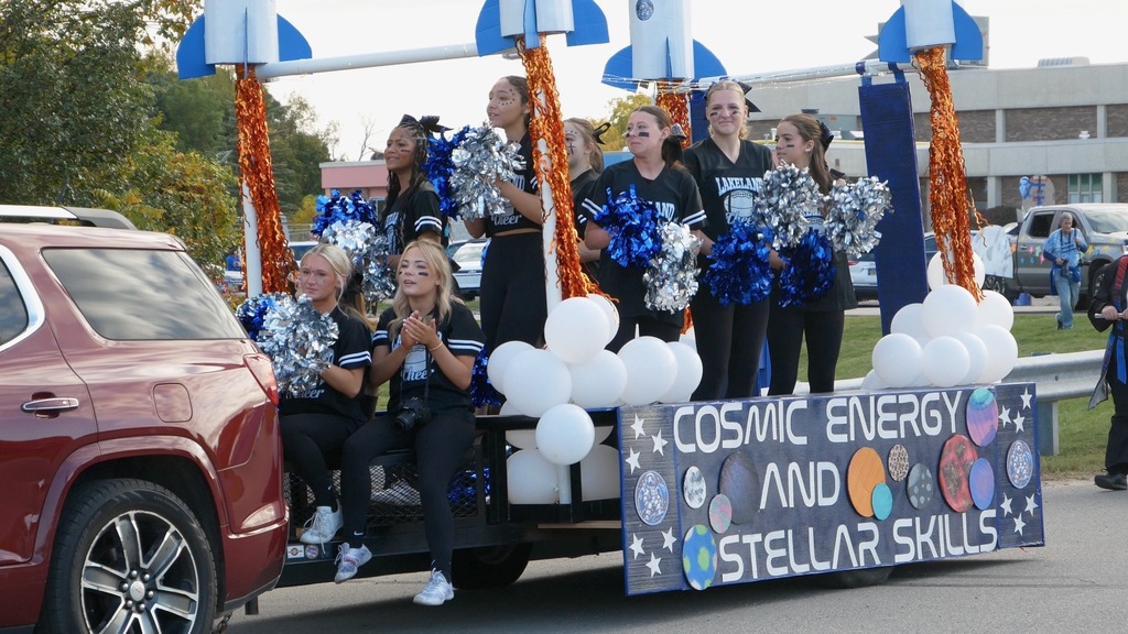 Teen girls holding pom pons riding trailer in a parade