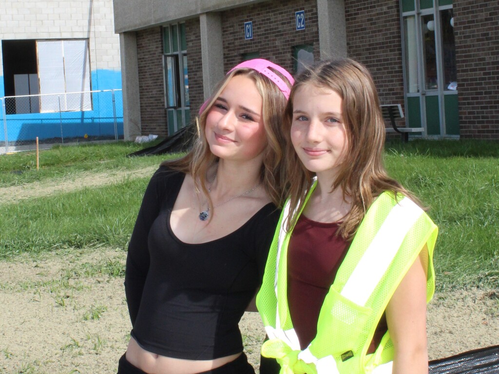 a pair of children smiling and posing for a photo outside a school wearing construction gear.