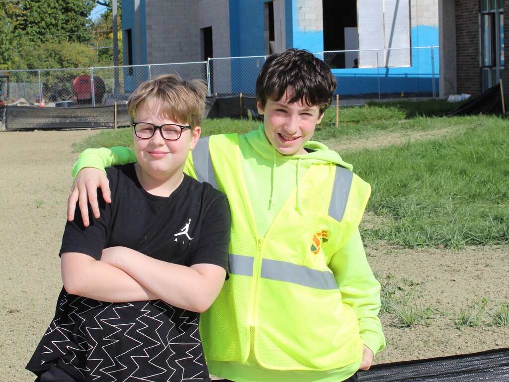 a pair of children smiling and posing for a photo outside a school wearing construction gear.