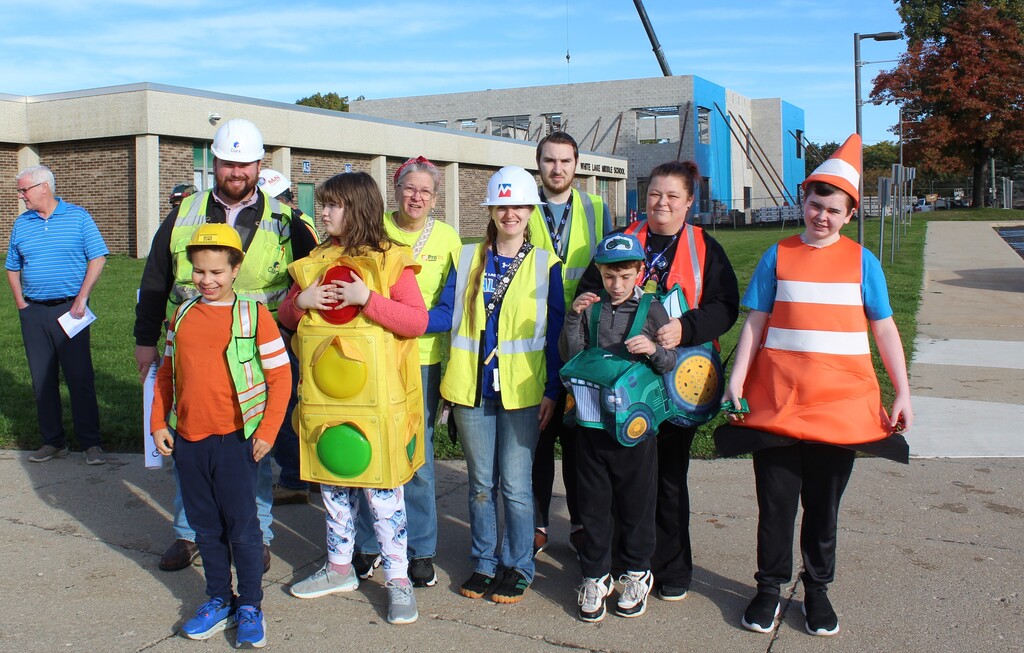 Group of adults and children smiling and posing for a photo outside a school. 