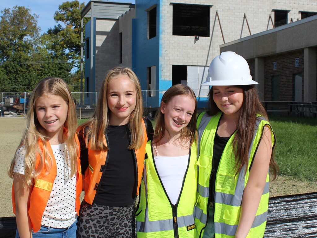 Four children smiling and posing for a photo outside a school wearing construction gear.