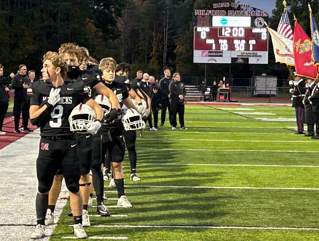 Football players lined up on the sideline for the national anthem with color guard