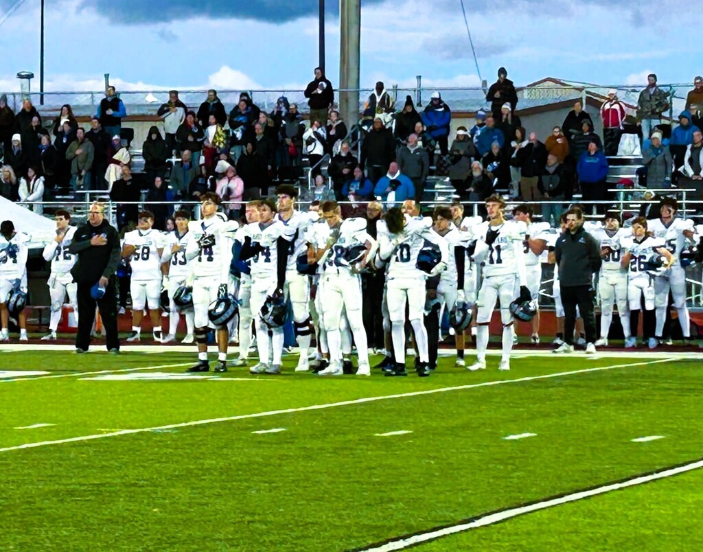 Football players standing at attention with hands over hearts during national anthem on football field