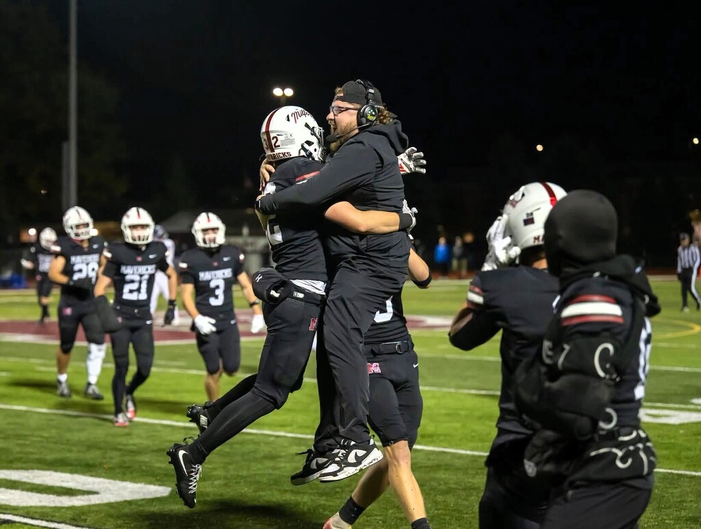 Player and coach leaping into a hug on the sidelines of a football field
