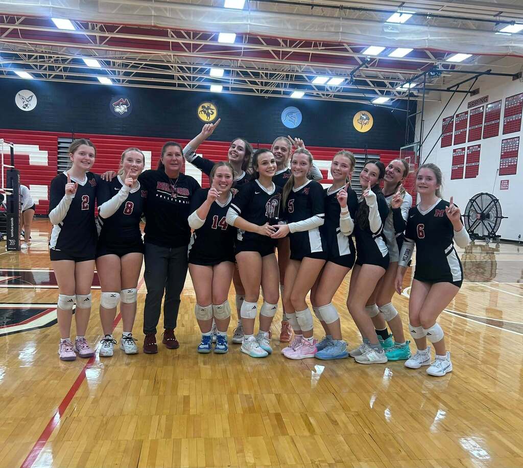 Team photo of girls freshmen volleyball team, smiling and posing for a photo on the court