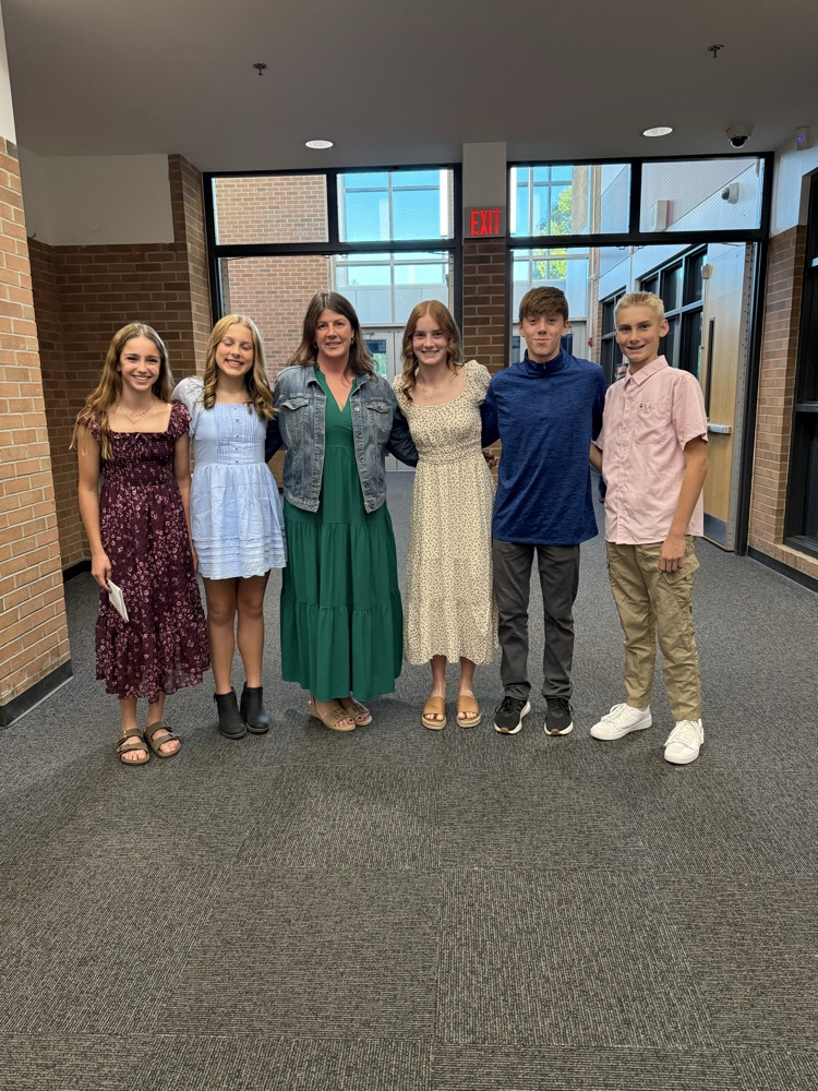 five students and one teacher stand in front of windows at the board meeting