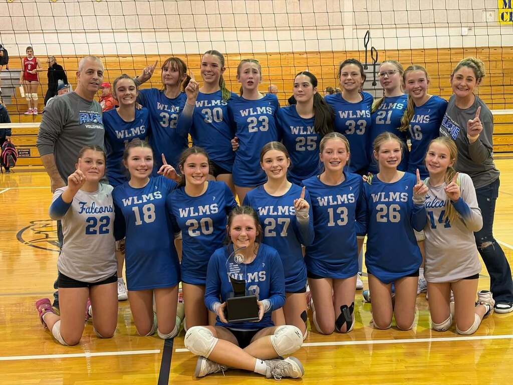 Photo of girls volleyball team smiling and posing for a picture in front of a volleyball net