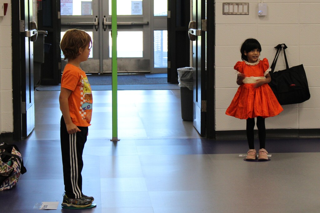 Two kids dressed in orange standing in a room 