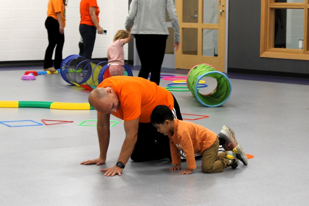 A an and a boy on their knees int he middle of a room while others play in the background
