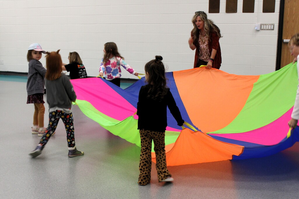 Several kids and an adult playing with a multi-colored parachute