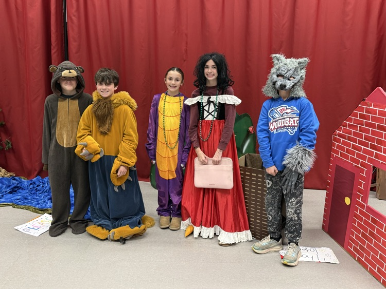 a group of students in costumes stand in front of a red curtain 