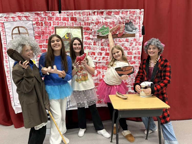 a group of students in costumes stand in front of a red curtain 