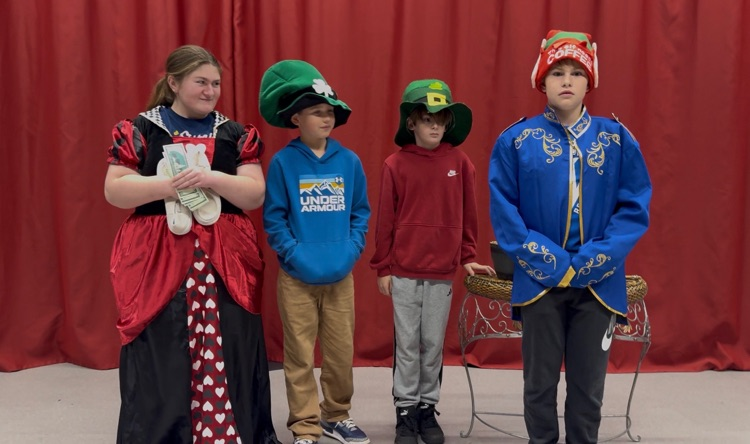 a group of students in costumes stand in front of a red curtain 